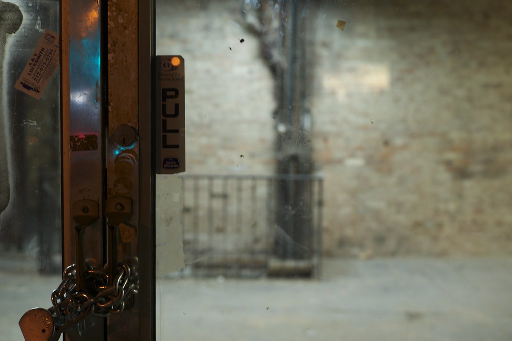 Old wooden door with a padlock and PULL sign opening onto a brick-walled room